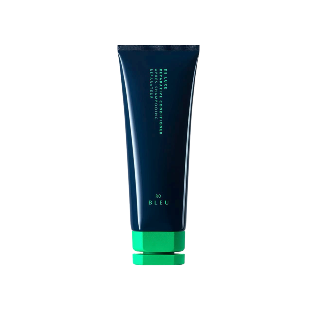 &quot;R+Co BLEU De Luxe Reparative Conditioner tube in navy blue with green cap, formulated for strengthening and hydrating damaged hair.