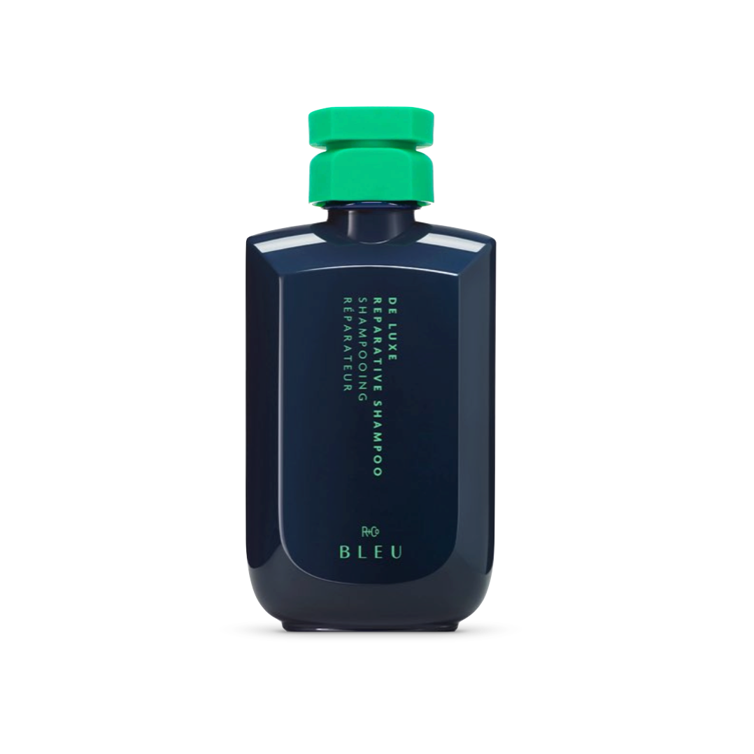 R+Co BLEU De Luxe Reparative Shampoo bottle in navy with a contrasting green cap, designed for deep repair and hydration of damaged hair.