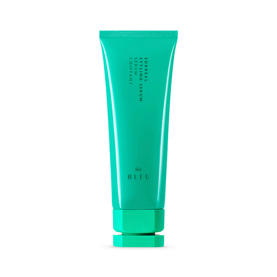 Bright jade colored tube of R+Co BLEU Surreal Styling Serum, a luxurious hair care product offering control and shine. The sleek packaging design reflects its premium quality, promising to leave hair with a flexible hold and a touchable, soft finish.