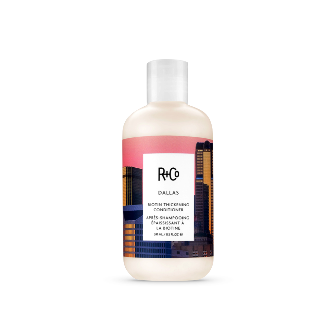 R+Co Dallas Biotin Thickening Conditioner bottle, 8.5 oz with a pink and blue Dallas cityscape design, for volumizing fine hair.