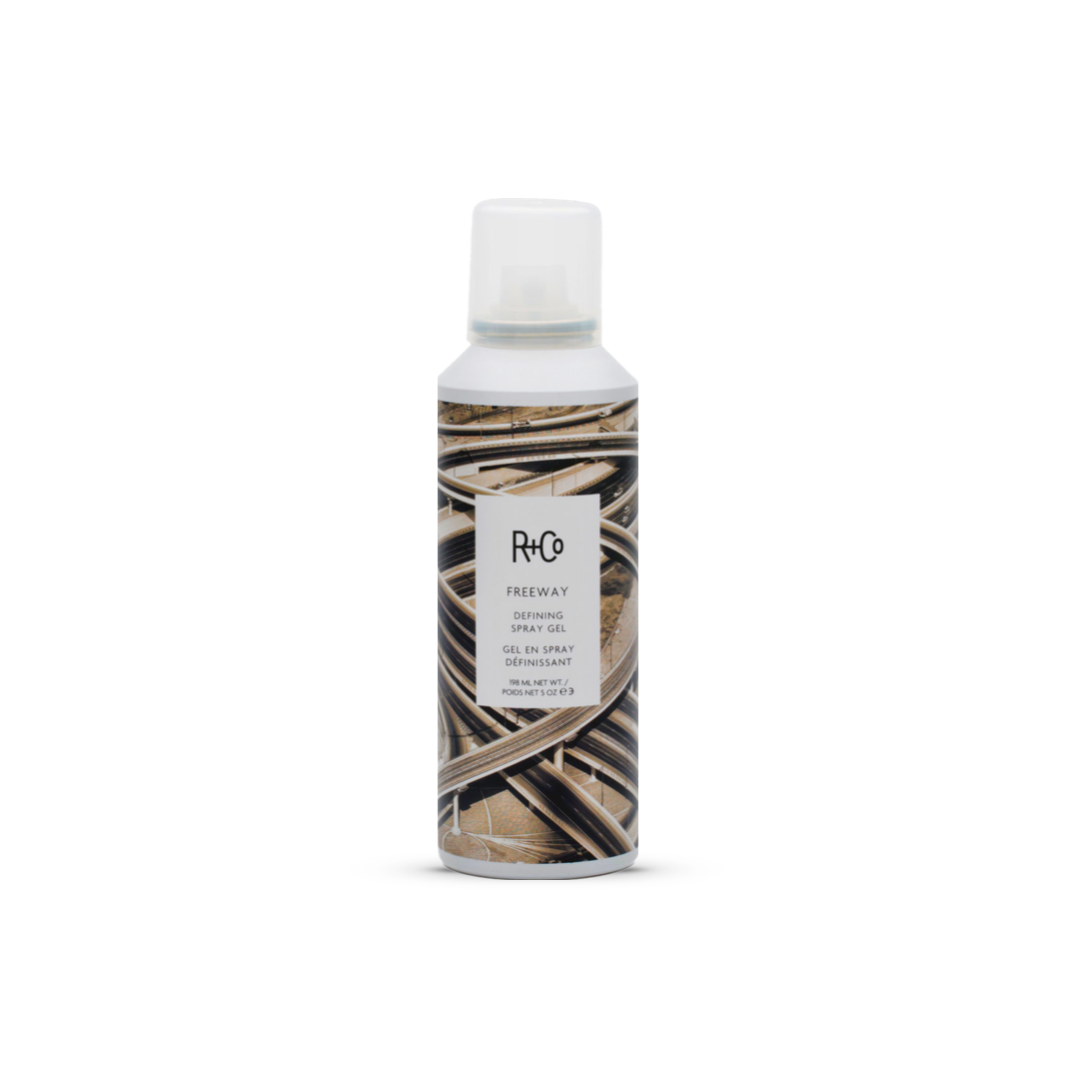 R+Co FREEWAY Defining Spray Gel in a spray bottle with a white cap and abstract highway design, 198ml, for creating volume and definition in all hair types.