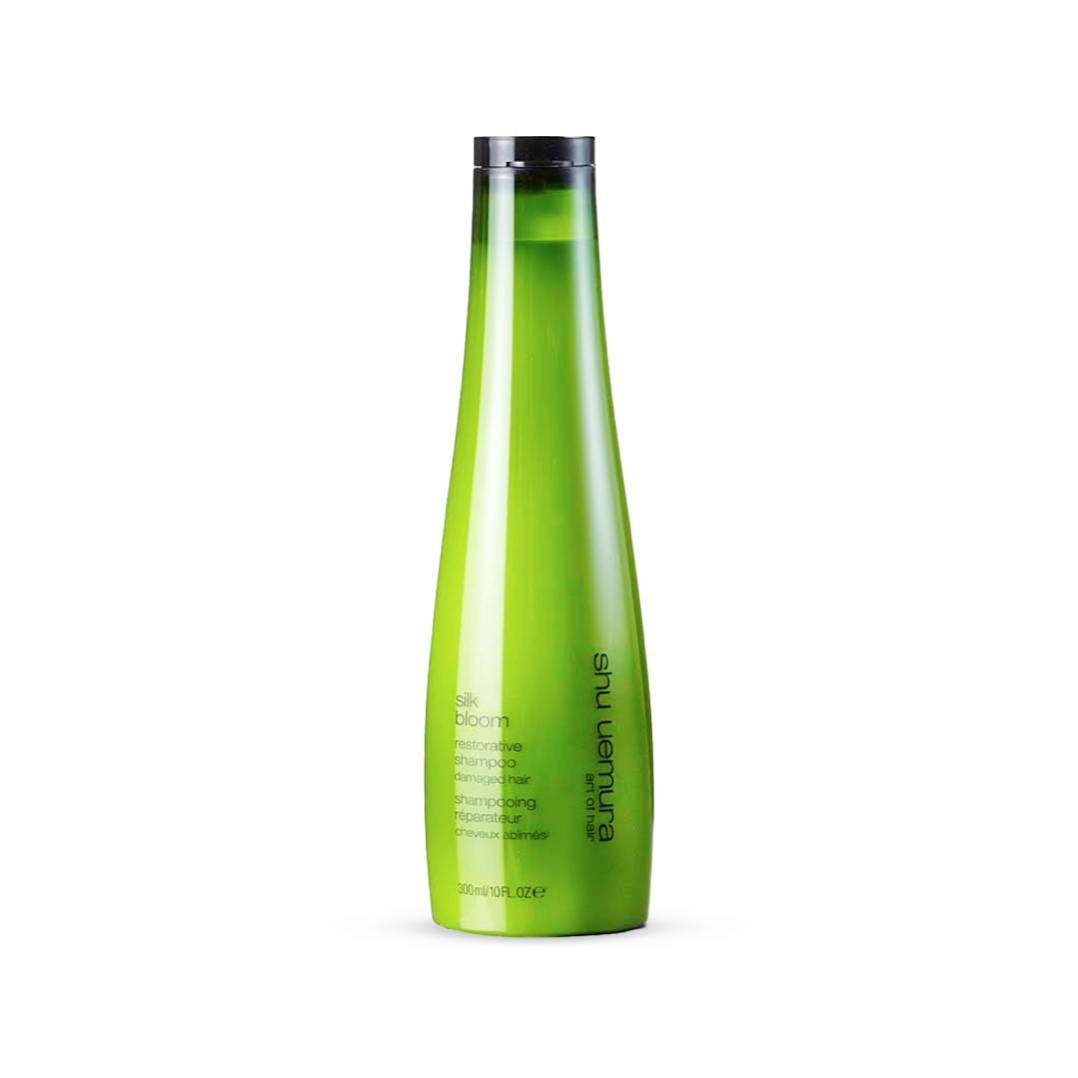 Tapered, luminous green bottle of Shu Uemura Silk Bloom Shampoo, 300ml/10fl.oz. The label is inscribed with elegant white lettering that details the restorative properties of the shampoo, designed specifically for damaged hair.